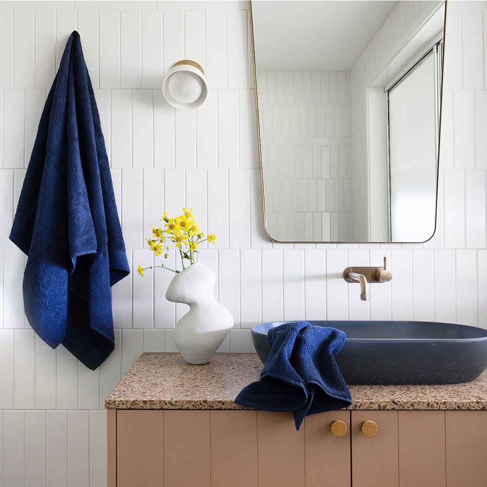 Navy towels in a modern bathroom with terrazzo counter, sculptural vase, and yellow flowers