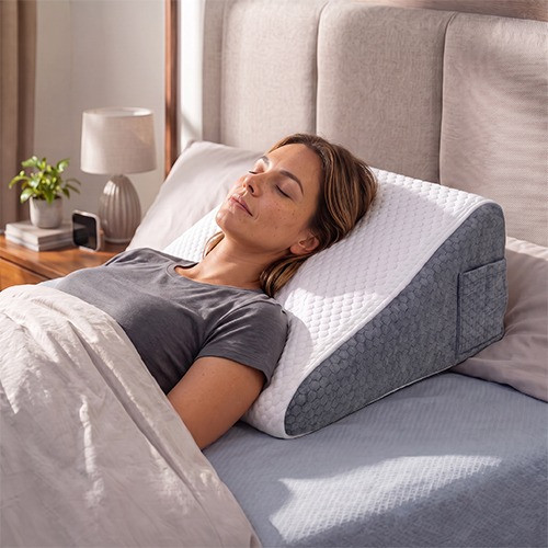 Woman reclining in bed with her legs elevated on a white foam wedge pillow