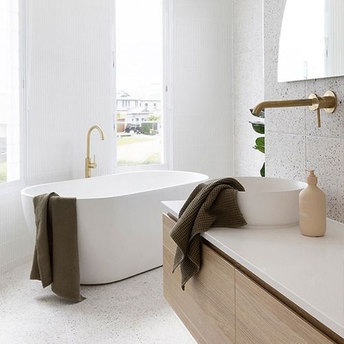 Bright bathroom with a freestanding white tub, vessel sink, gold fixtures, and dark towels draped over the tub and counter