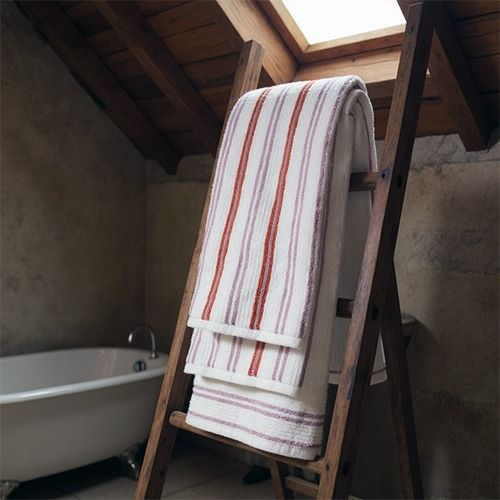 Striped towels hanging on a wooden ladder rack in a rustic bathroom with a skylight and clawfoot bathtub.