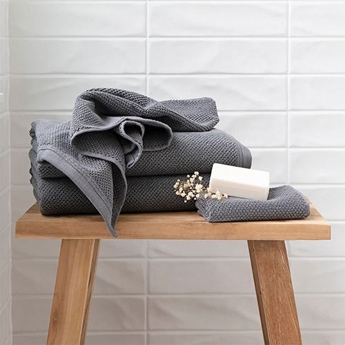 Folded gray waffle-textured towels on a wooden bench with a white bar soap and dried flowers